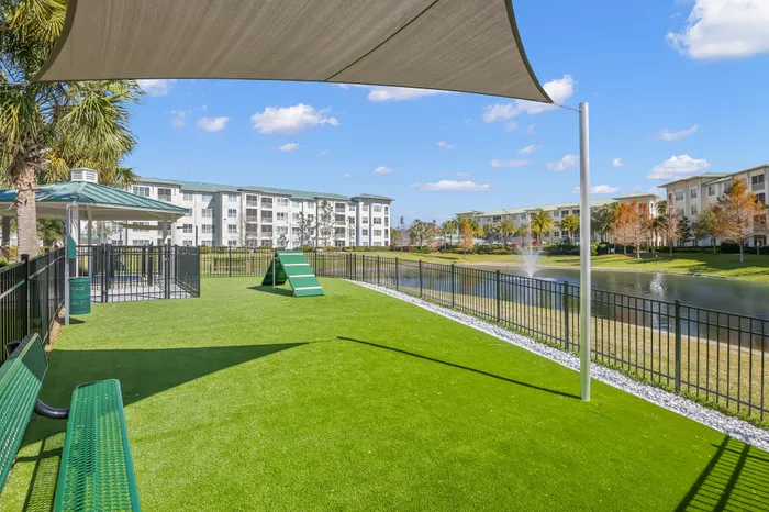 Inviting apartment complex with a pristine dog park, vibrant greenery, and tranquil pond view.