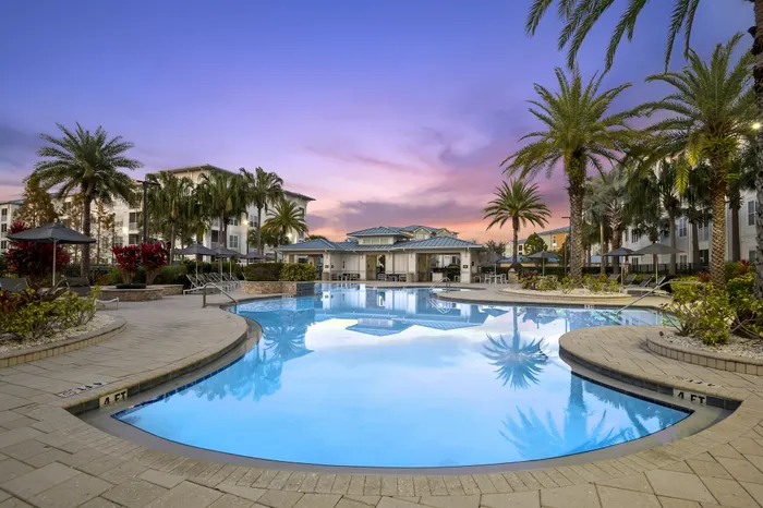 Luxurious apartment complex showcasing a stunning pool area surrounded by palm trees at sunset, offering a tropical oasis feel.
