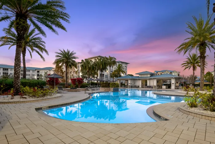 Luxurious apartment complex with shimmering pool, surrounded by lush palm trees and vibrant sunset skies.