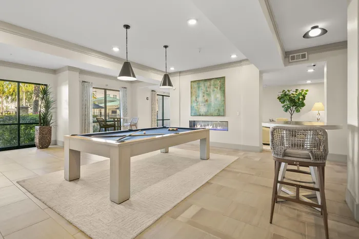 Elegant entertainment room featuring a modern pool table, cozy fireplace, and stylish decor with abundant natural light.