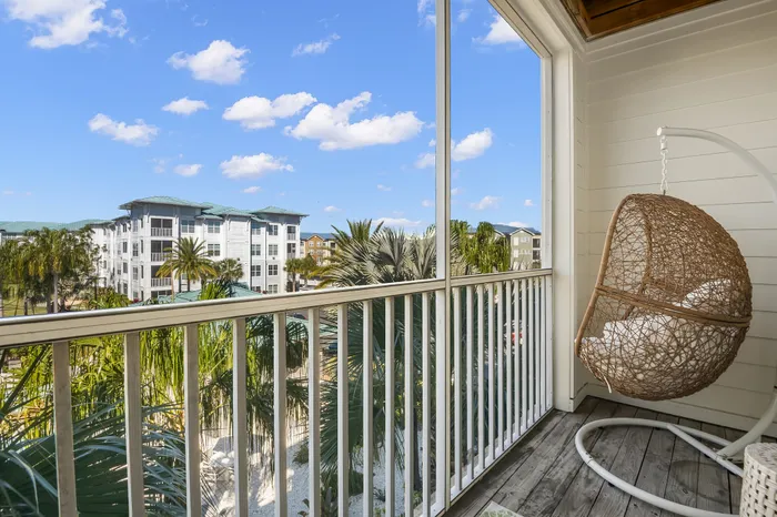 Charming balcony with a cozy hanging chair overlooking tropical greenery and a vibrant residential complex under a bright blue sky.