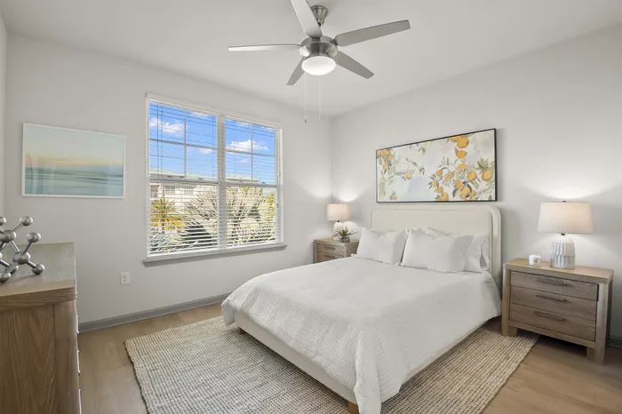 Bright and airy bedroom featuring a cozy bed, stylish artwork, natural wood furnishings, and large windows with a refreshing view.