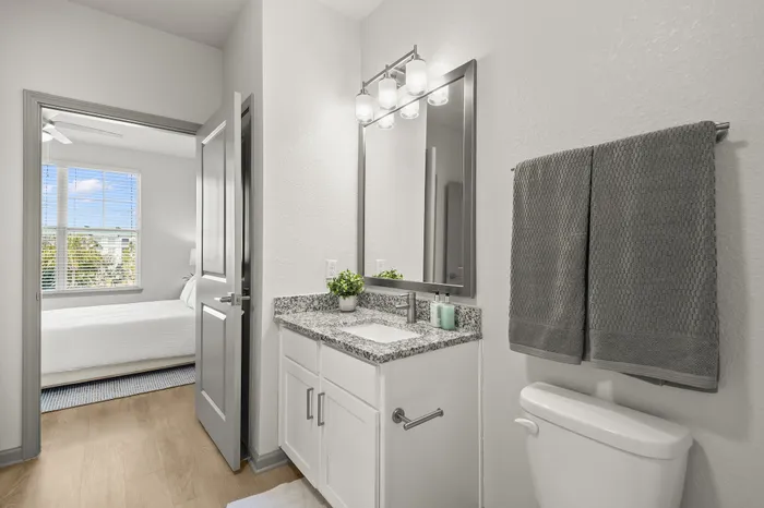 Bright modern bathroom with elegant granite countertop and view into a cozy, sunlit bedroom.