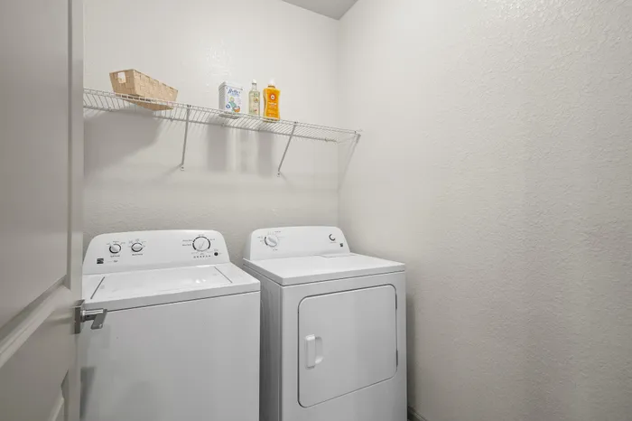 Charming laundry room featuring modern washer and dryer units with convenient shelving for storage.
