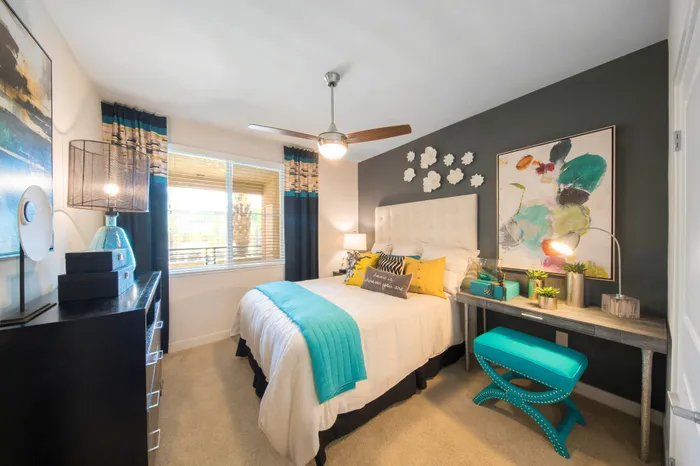 Chic and cozy bedroom with modern decor, featuring a plush bed adorned with vibrant teal and yellow accents, complemented by contemporary artwork and natural light.