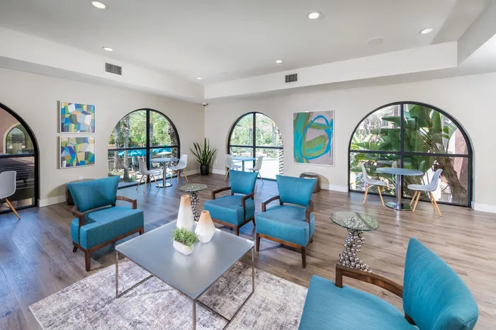 Elegant living area with vibrant blue chairs, contemporary art, and large arched windows overlooking lush greenery.