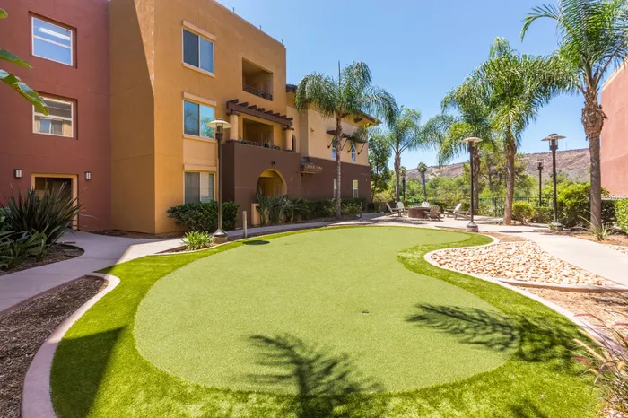 Charming apartment exterior with vibrant landscaping, palm trees, and a cozy patio area under a clear blue sky.