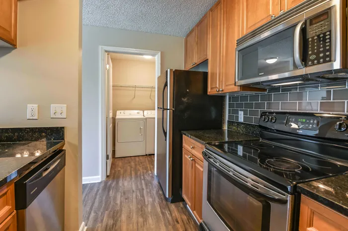 Elegant kitchen with modern stainless steel appliances, sleek granite countertops, and warm wooden cabinetry, seamlessly connected to a convenient laundry area.