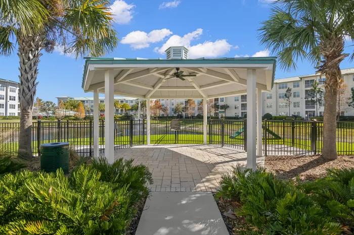 Charming gazebo set in lush greenery with apartment buildings in the background, offering a serene outdoor space for relaxation.