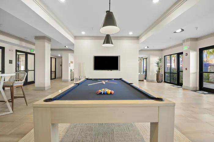 Luxurious apartment recreation room featuring a sleek pool table, stylish seating, and ample natural light for a perfect leisure escape.