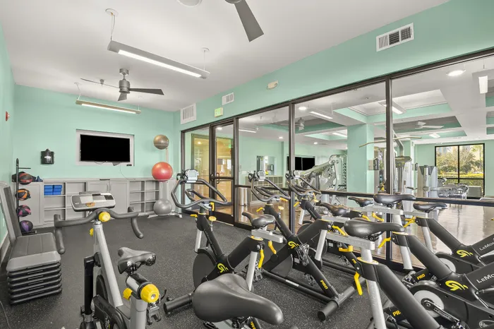 Modern fitness room with stationary bikes, bright interior, and large windows for natural light.