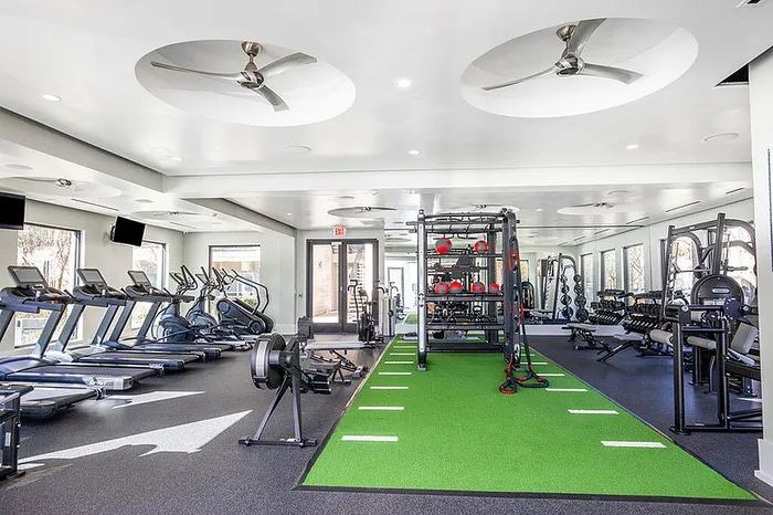 Spacious, modern gym featuring state-of-the-art cardio machines, weight training equipment, and vibrant green turf for functional workouts.
