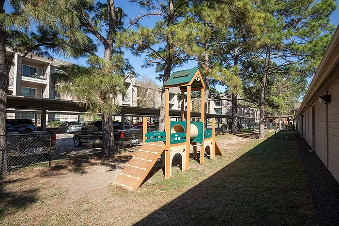 Charming apartment community with a well-maintained pet playground, surrounded by lush trees and ample parking.