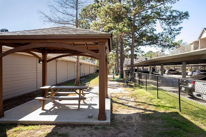 Charming outdoor area with a wooden gazebo and picnic table, nestled between tall pine trees, offering a serene retreat.