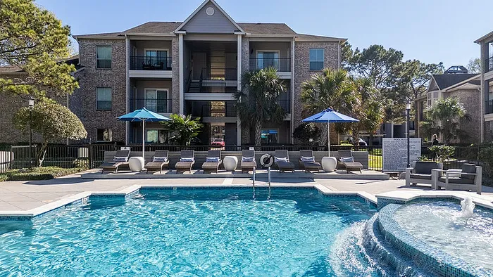 Inviting apartment complex with a sparkling swimming pool, surrounded by sun loungers and lush greenery, perfect for relaxation and leisure.