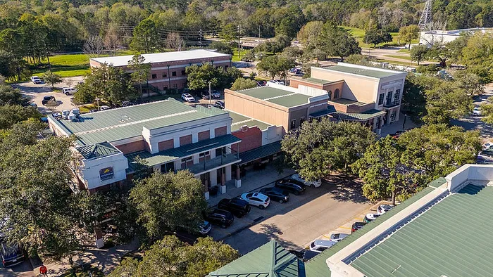 Charming aerial view of a commercial complex surrounded by lush greenery, featuring modern buildings with green rooftops and ample parking.