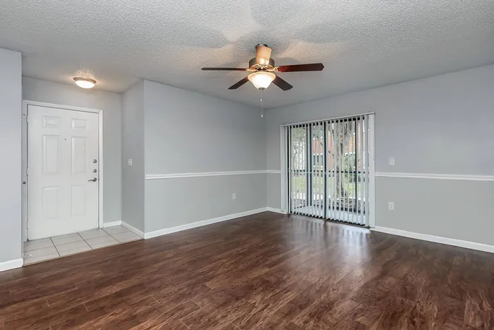 Inviting living space featuring elegant wood flooring, modern ceiling fan, and ample natural light through sliding glass doors.