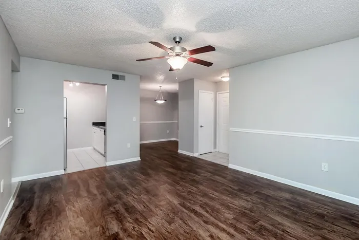 Bright living space with elegant hardwood flooring, open entry to a modern kitchen, and ceiling fan lighting.