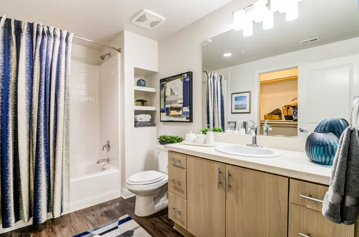 Elegant bathroom with modern fixtures, featuring a chic vanity, stylish wall art, and a refreshing blue shower curtain.