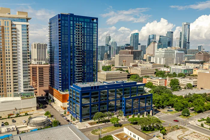 Stunning urban skyline showcasing a modern high-rise building with blue accents, surrounded by vibrant cityscape and lush greenery.
