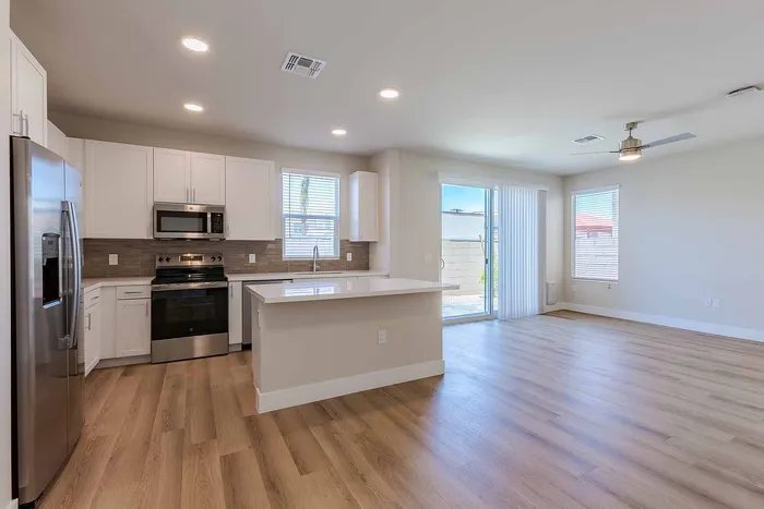 Bright and modern open-concept kitchen with sleek stainless steel appliances, elegant white cabinetry, and spacious hardwood floored living area.