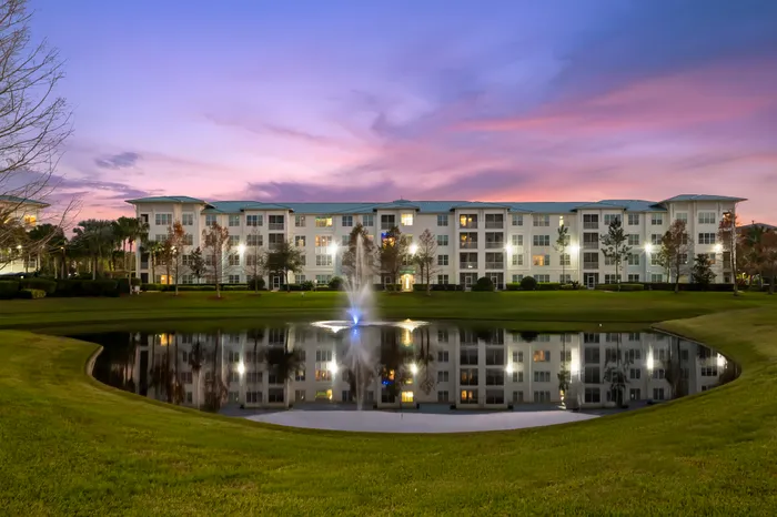 Luxurious lakeside apartment complex at dusk, featuring a beautiful sunset sky and elegant water fountain reflection.