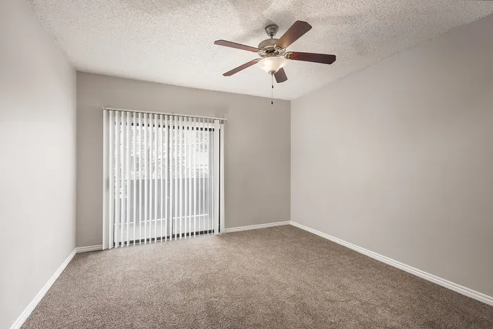 Bright and airy room with plush carpet, modern ceiling fan, and sliding glass doors leading to a private balcony, perfect for relaxation and comfort.