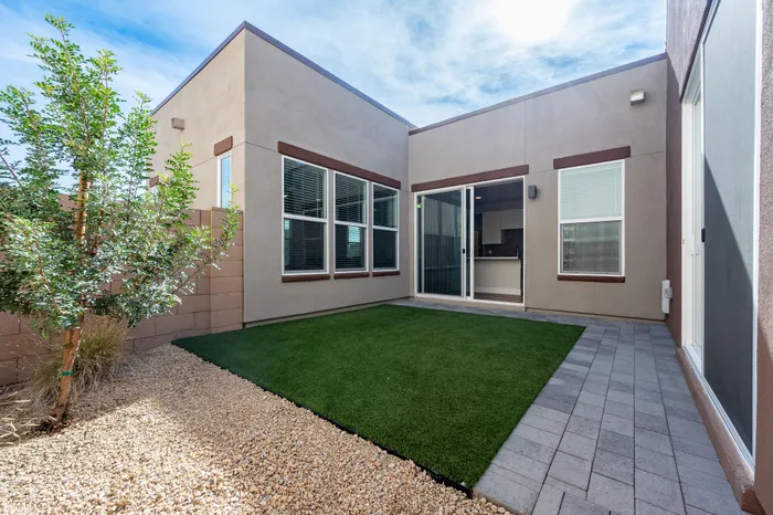 Charming modern apartment featuring a spacious patio with lush green grass, stone pathway, and large sliding glass doors for natural light.