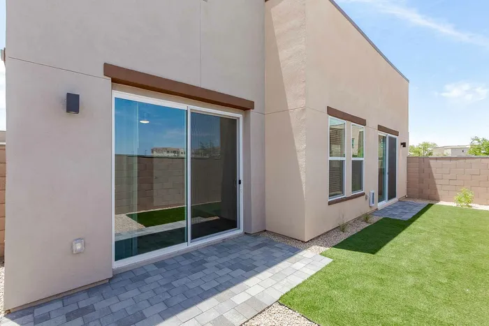 Inviting backyard with modern sliding glass doors opening to a sleek patio and lush green lawn, perfect for relaxation and outdoor activities.