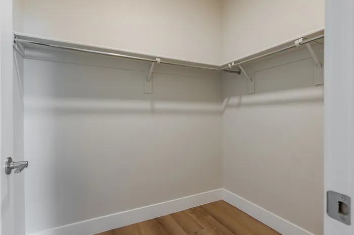 Spacious walk-in closet featuring sleek wooden flooring and modern shelving, ideal for stylish storage solutions.
