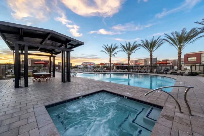 Luxurious outdoor pool area at sunset with palm trees, modern lounge chairs, and inviting hot tub, perfect for relaxation and entertainment.