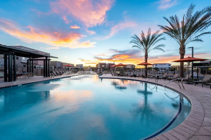 Luxurious swimming pool area with palm trees and modern lounge chairs at sunset, ideal for relaxation and leisure.