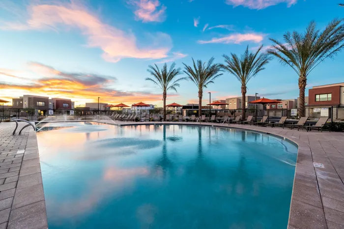 Luxurious apartment complex featuring a stunning outdoor pool with palm trees and a vibrant sunset backdrop.