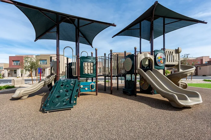Modern playground with slides and climbing structures in a community setting under blue skies.