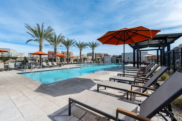 Luxurious outdoor pool area with modern lounge chairs and vibrant orange umbrellas, surrounded by palm trees and contemporary architecture.