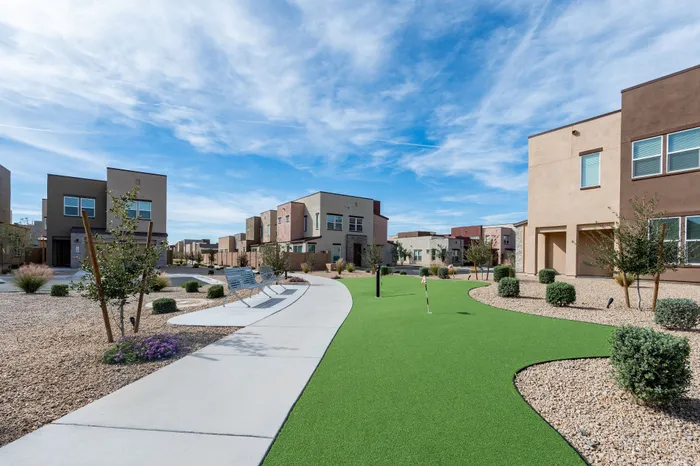 Modern residential community with stylish townhouses, vibrant landscaping, and a scenic putting green under a clear blue sky.