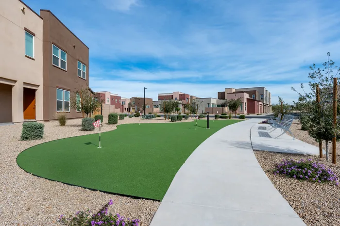 Inviting modern apartment complex with vibrant landscaping and a fun putting green under a clear blue sky.