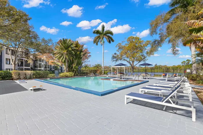 Luxurious outdoor pool area with sleek lounge chairs, surrounded by lush tropical greenery and clear blue skies, perfect for relaxation and leisure.
