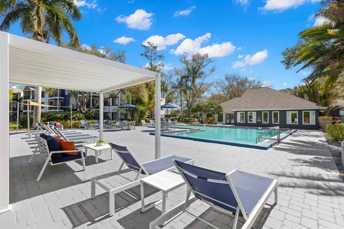 Resort-style apartment complex with a luxurious outdoor pool, surrounded by modern lounge chairs and lush palm trees.