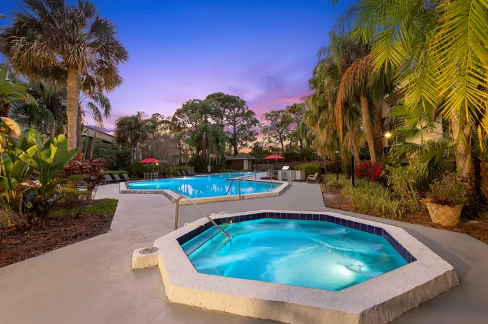 Serene outdoor pool area at sunset with lush palm trees, inviting hot tub, and vibrant foliage.