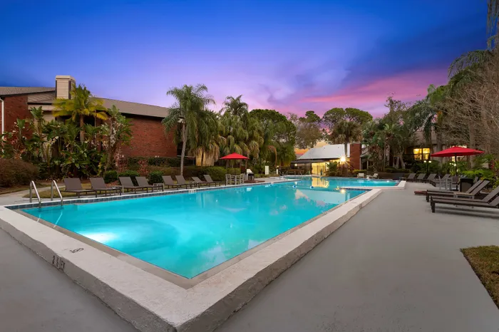 Luxurious outdoor pool area with palm trees and sunset views, featuring ample lounge chairs and lush surroundings.