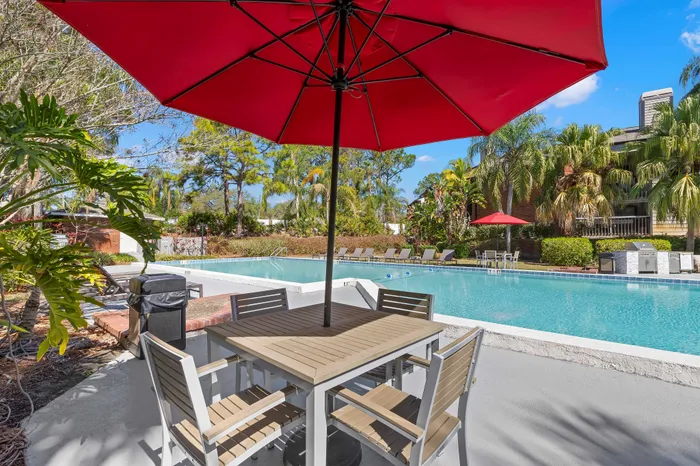 Inviting outdoor space with a stunning pool, sunlit lounge chairs, and lush tropical landscaping, perfect for relaxation under a vibrant red umbrella.