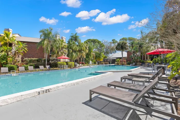 Luxurious outdoor swimming pool surrounded by lush greenery and stylish lounge chairs, offering a perfect relaxation spot under the clear blue sky.