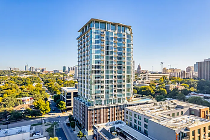 Modern high-rise building with sleek glass facade, offering panoramic city views surrounded by lush greenery and urban skyline.