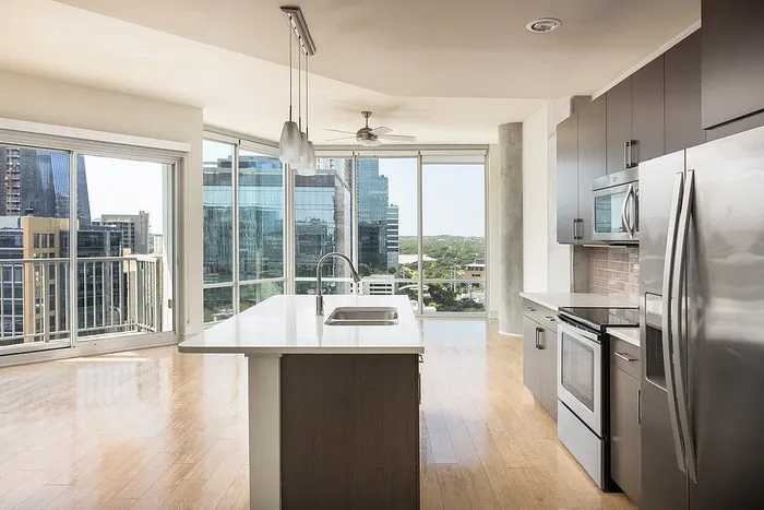 Contemporary kitchen with sleek appliances, an elegant island, and panoramic city views from floor-to-ceiling windows.