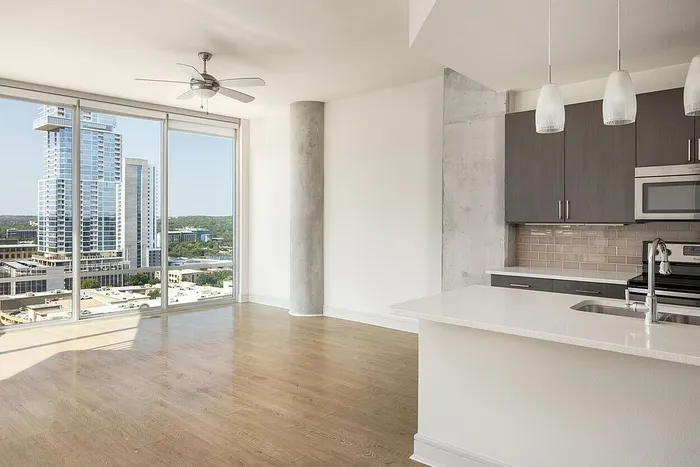 Modern apartment with floor-to-ceiling windows offering breathtaking city views, featuring an open-plan kitchen with sleek cabinetry and stainless steel appliances.