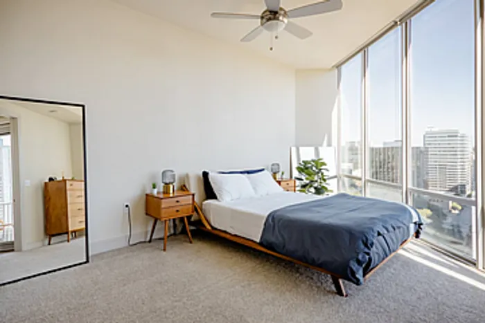 Bright and modern bedroom with floor-to-ceiling windows showcasing stunning city views, elegant furnishings, and ambient lighting.