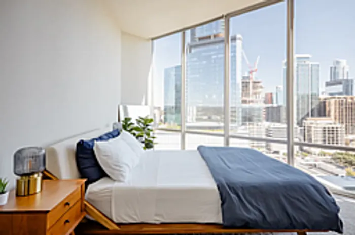Bright and modern bedroom with floor-to-ceiling windows offering stunning city views and contemporary decor.