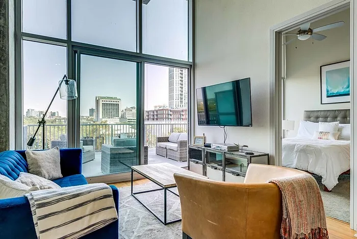 Bright and modern living space with a cozy living room, sleek furniture, and a view of the city skyline from a private balcony.