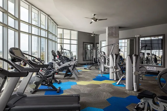 Modern gym with floor-to-ceiling windows, state-of-the-art fitness equipment, and vibrant geometric flooring.